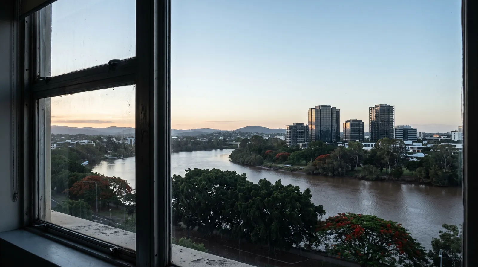 View from an office window across a subtropical river city at dawn.