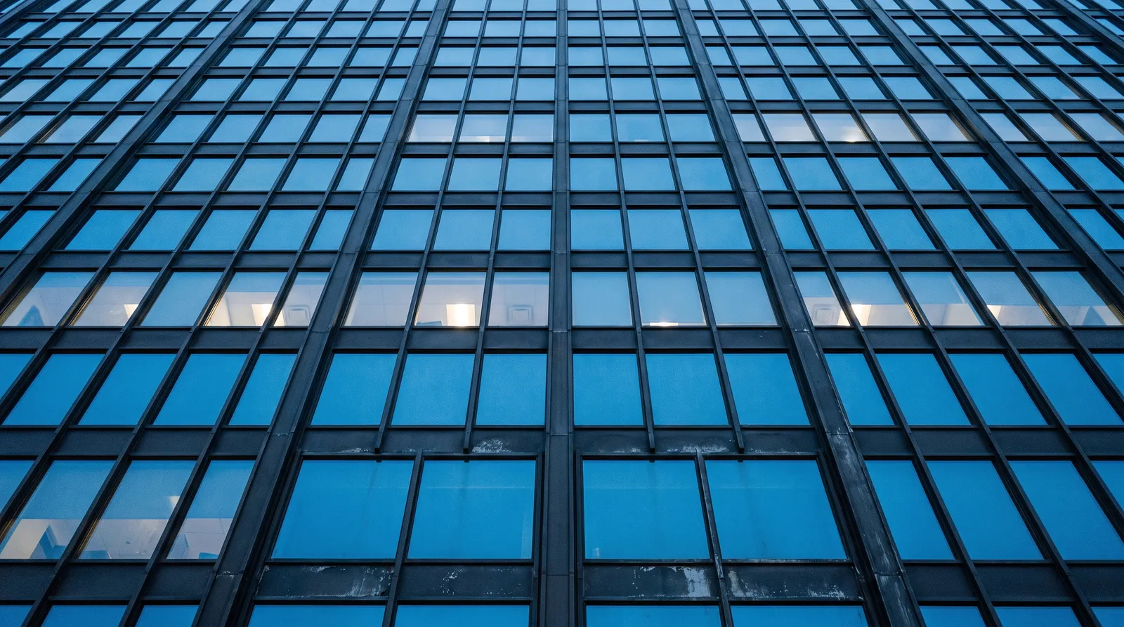 Looking up the glass facade of an office tower at blue hour.